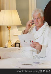 Businessman Reading and Phoning in Bed