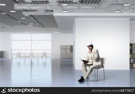 Businessman reading book. Elegant businessman in white suit sitting on chair in office interior