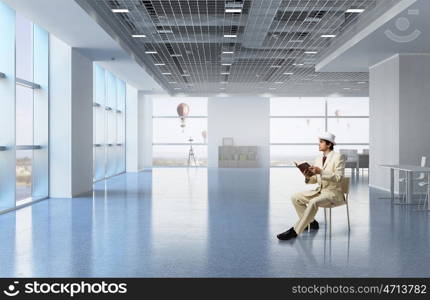 Businessman reading book. Elegant businessman in white suit sitting on chair in office interior