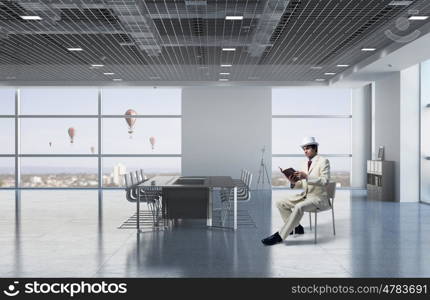 Businessman reading book. Elegant businessman in white suit sitting on chair in office interior