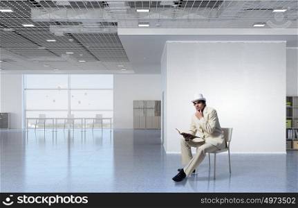 Businessman reading book. Elegant businessman in white suit sitting on chair in office interior