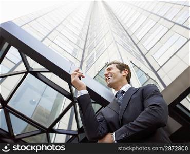 Businessman reading message on phone outside office (low angle view)