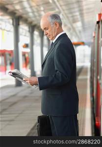 Businessman Reading Newspaper at Train Station