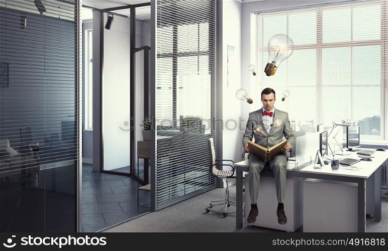 Businessman reading old book. Businessman in office sitting on table and reading old book