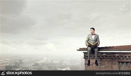 Businessman reading old book. Young businessman reading book sitting on roof of building