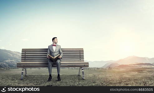 Businessman reading old book. Young businessman wearing red bow tie sitting on bench with book in hands