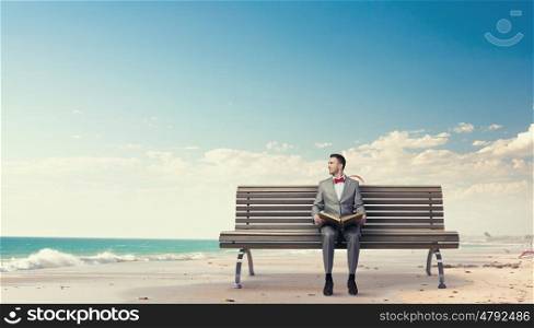 Businessman reading old book. Young businessman wearing red bow tie sitting on bench with book in hands