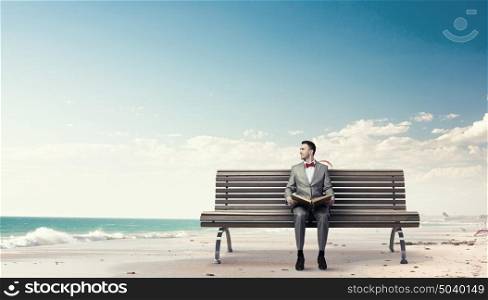 Businessman reading old book. Young businessman wearing red bow tie sitting on bench with book in hands