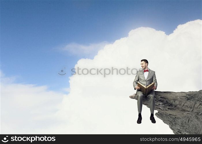 Businessman reading old book. Young handsome businessman on rock edge with old book in hands