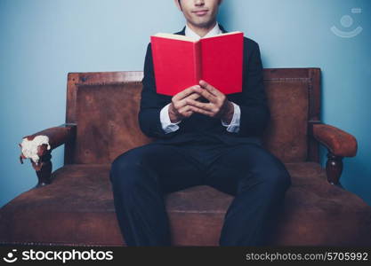 Businessman reading red book on sofa