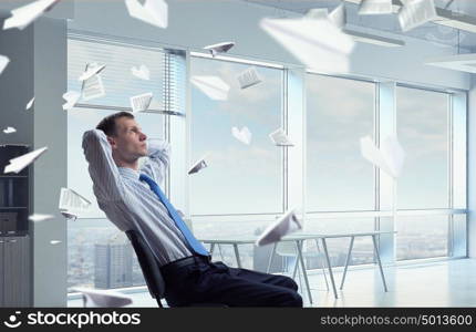 Businessman relaxing in his office mixed medi. Relaxed businessman at the office sitting back with his hands behind his head