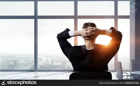 Businessman relaxing in his office mixed media. Relaxed businessman at the office sitting back with his hands behind his head