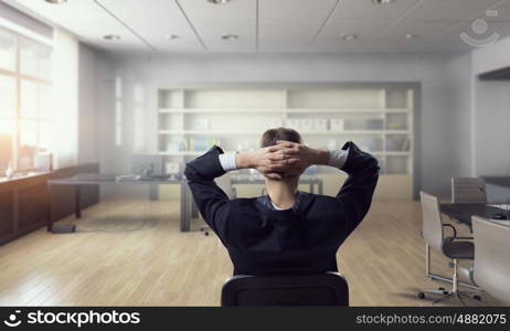 Businessman relaxing in his office mixed media. Relaxed businessman at the office sitting back with his hands behind his head