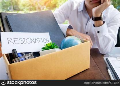 Businessman resignation packing up all his personal belongings and files into a brown cardboard box.