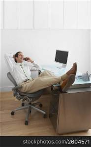 Businessman resting his legs on the desk and talking on a mobile phone in an office