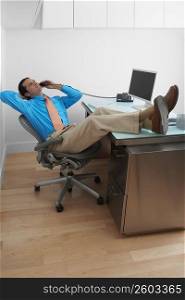 Businessman resting his legs on the desk and talking on the telephone in an office