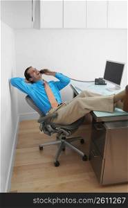 Businessman resting his legs on the desk and talking on the telephone in an office