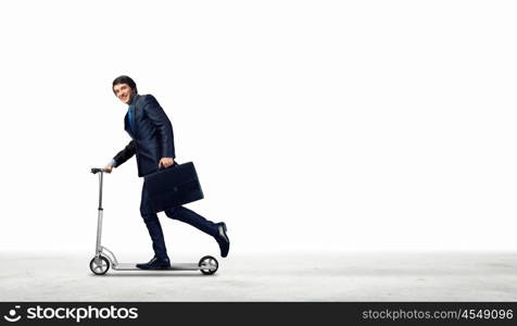 Businessman riding scooter. Image of young businessman in black suit riding scooter