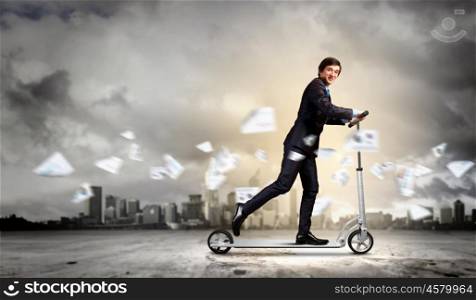 Businessman riding scooter. Image of young businessman in black suit riding scooter