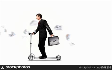 Businessman riding scooter. Image of young businessman in black suit riding scooter
