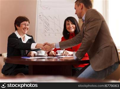 Businessman rising to his feet and shaking hands with a smiling woman executive after a meeting seated around a table as they reach an agreement, congratulate each other or in greeting