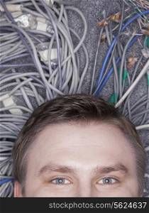 Businessman&rsquo;s face lying down on computer cables looking up, half