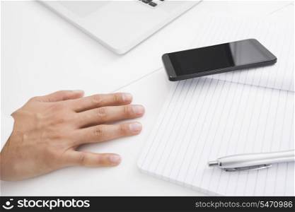 Businessman&rsquo;s hand on desk by cell phone; pen and book