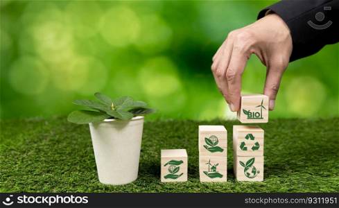 Businessman’s hand holding eco-concern symbol on wooden cube and plant pot. Eco-friendly bio fuel from plants or waste for alternative sustainable and clean bio energy to preserve eco future. Alter. Businessman’s hand holding eco-concern symbol and plant pot. Alter
