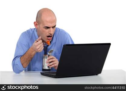 Businessman sat at desk eating from tin can