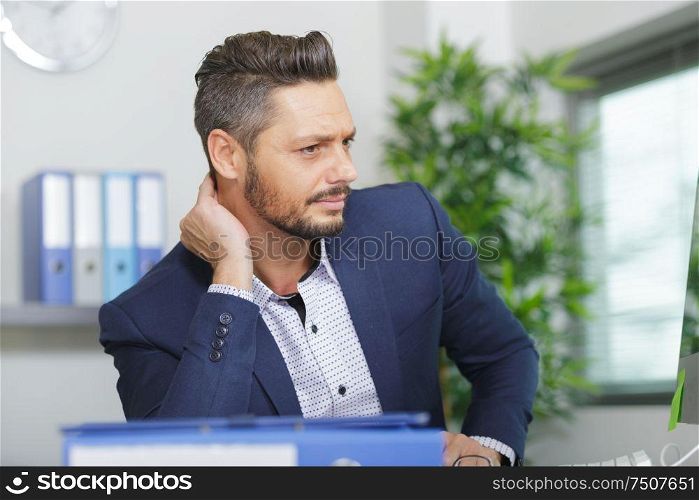 businessman sat at desk holding his neck
