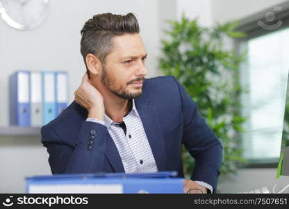 businessman sat at desk holding his neck