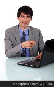 Businessman sat at desk pointing to laptop