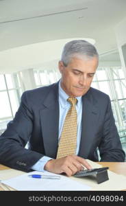 Businessman Seated at His Desk Using Calculator in office setting