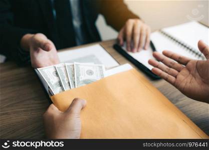 Businessman secretly giving a bribe by giving money bills in envelope contract document.