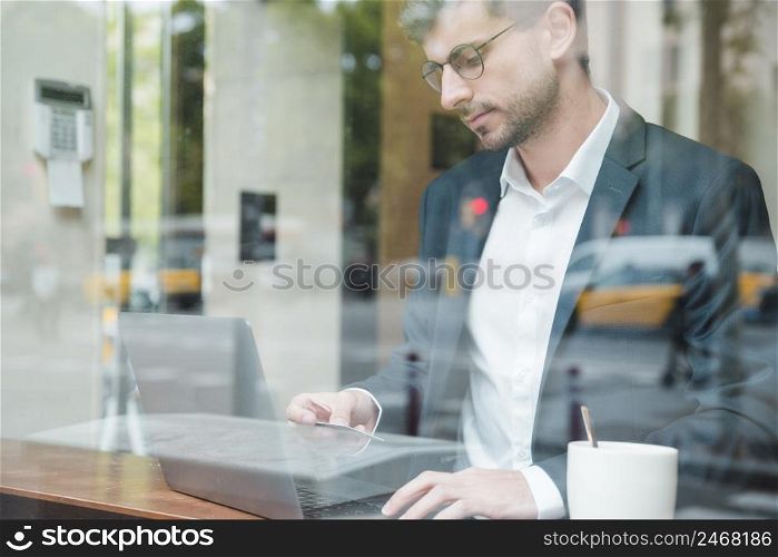 businessman seen through glass using credit card shopping online cafe