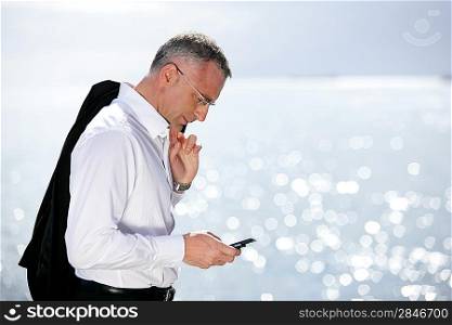 Businessman sending a text message by the seaside