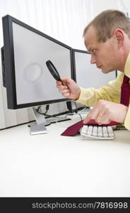 Businessman seriously analyzing data on a computer monitor using a magnifying glass, with his left index finger hovering above the escape key to interrupt the process.clipping path of the monitors is included at the maximum resolution of the image