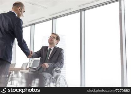 Businessman shaking hands with smiling disabled colleague in boardroom during meeting at office
