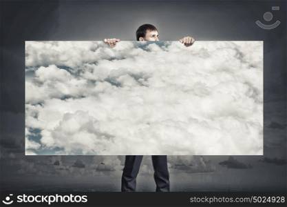 Businessman showing banner. Young businessman holding banner with blue cloudy sky