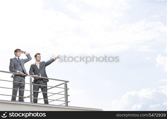 Businessman showing something to coworker against cloudy sky