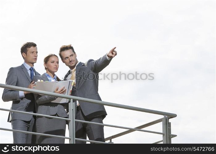 Businessman showing something to coworkers on terrace against sky