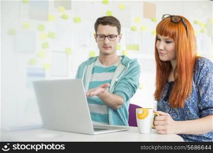 Businessman showing something to female colleague on laptop in creative office