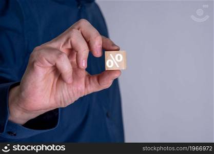 Businessman shows a wooden cube with a percent or percentage symbol. Business finance concept.. Businessman shows a wooden cube with a percent or percentage symbol.