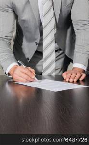 Businessman signing a contract. Businessman signing a contract standing near office desk