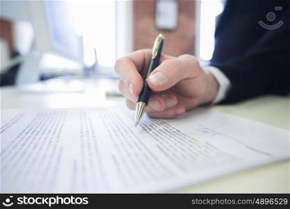 Businessman signing a contract. Businessman sitting at office desk signing a contract with shallow focus on signature and pen