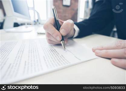 Businessman signing a contract. Businessman sitting at office desk signing a contract with shallow focus on signature.
