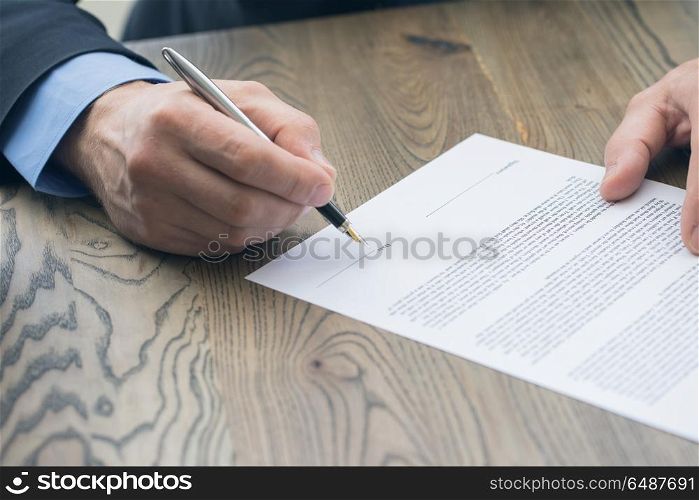 Businessman signing a contract. Businessman sitting at office desk signing a contract with shallow focus on date