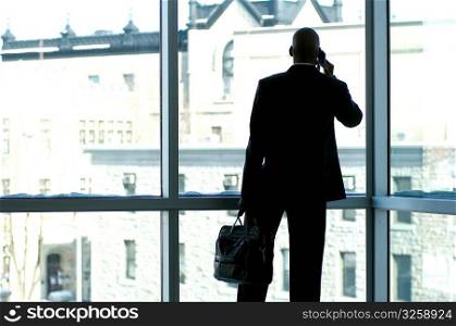 Businessman silhouetted in large office window.