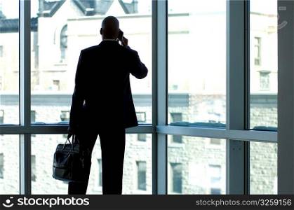Businessman silhouetted in large office window.