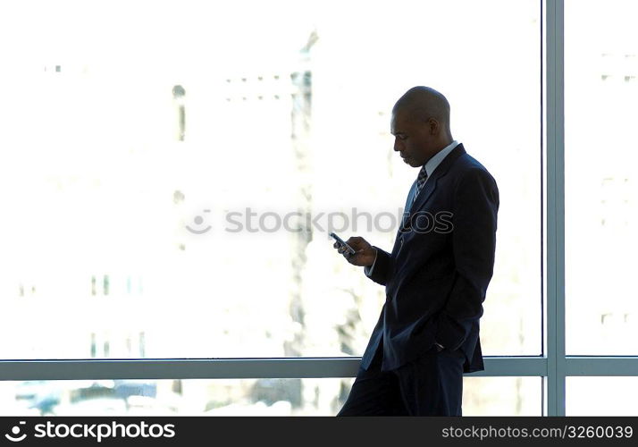 Businessman silhouetted in large office window, using PDA smart phone.